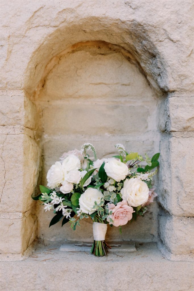 Classic petit sized Bridal bouquet with blush and white garden roses sitting in a stone alcove.