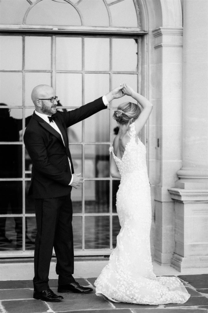 Groom gives bride a twirl in black and white in front of a window