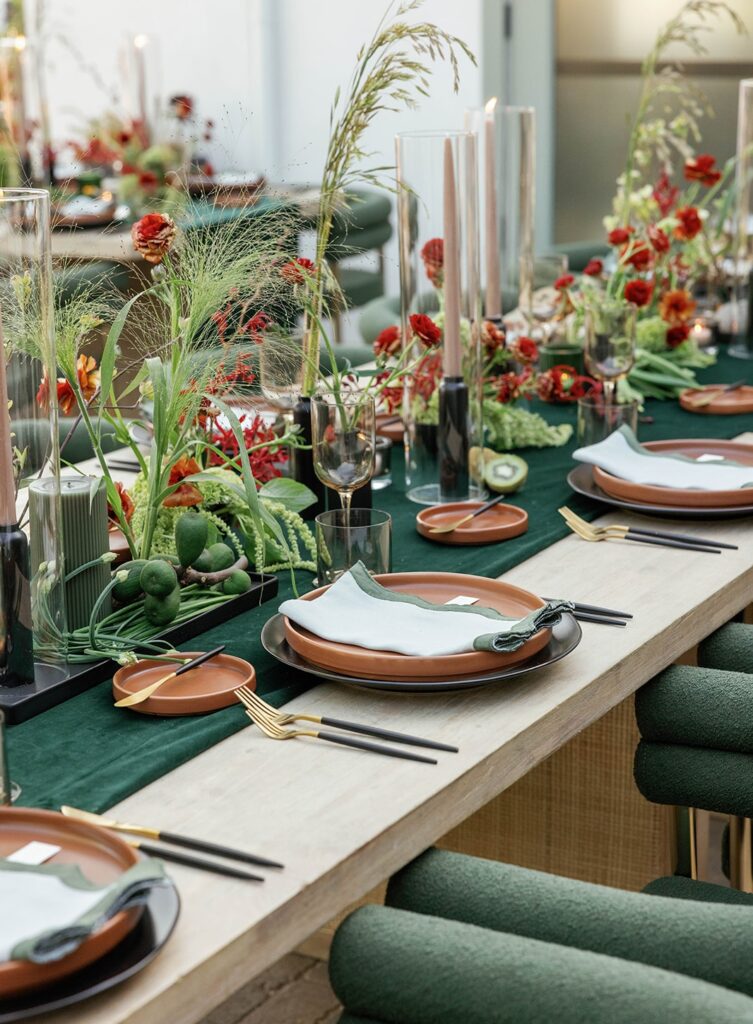 Detail of a modern wedding reception table styled with green velvet runners, terracotta plates, black flatware, and lush red florals. A bold and refined tablescape that reflects a unique wedding style florists can use to stand out and attract discerning clients.